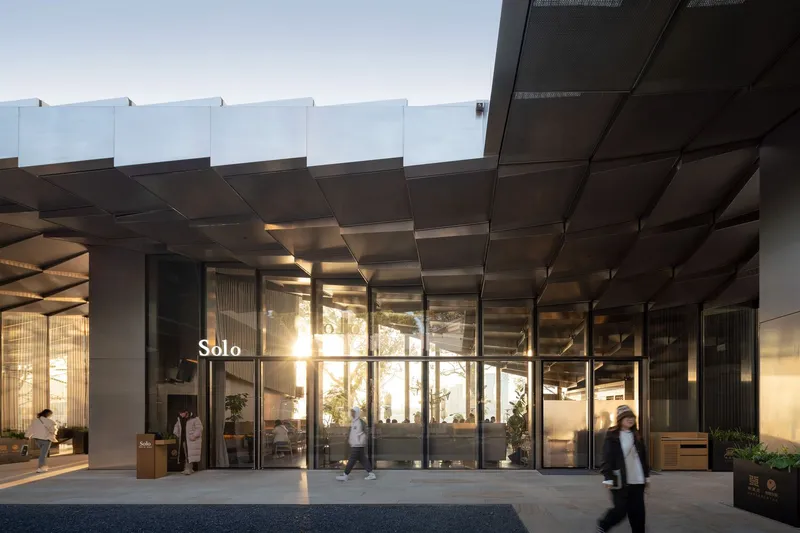 Entrance canopy with layered metal panels extending over glazed doors at dusk