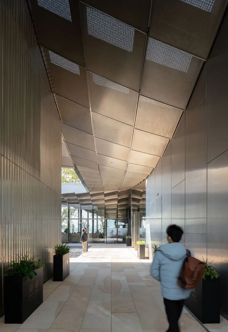Interior corridor with folded metal ceiling panels and perforated vents above pedestrians walking through