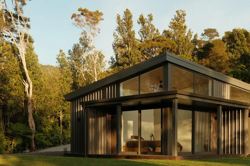 Corner view of the glazed facade with timber battens and black steel framing beneath trees