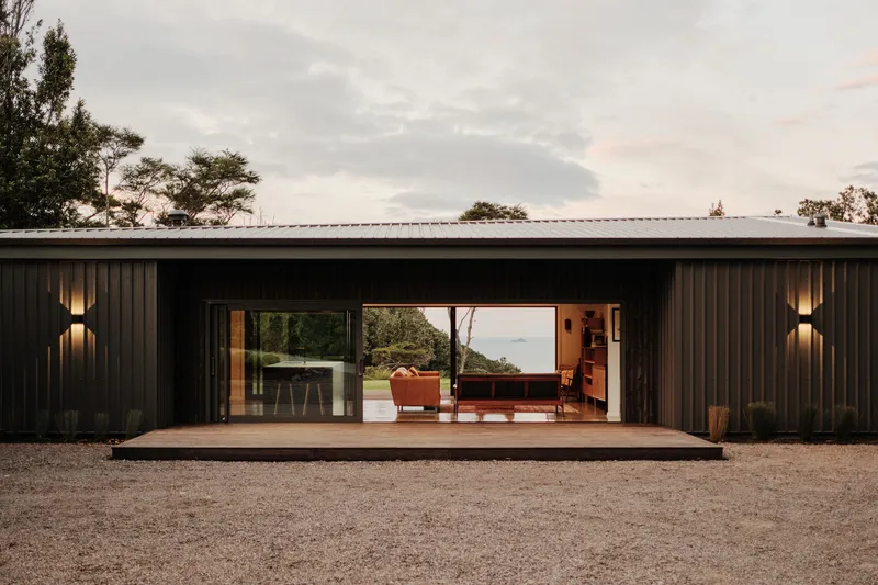 Vertical-clad facade with central sliding doors opening to a timber deck under evening sky
