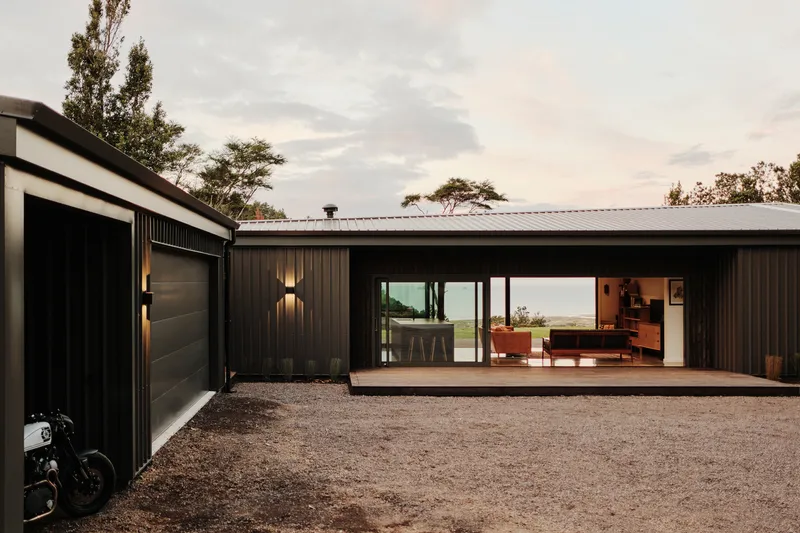 Dark vertical timber cladding with recessed living area opening onto gravel courtyard at dusk