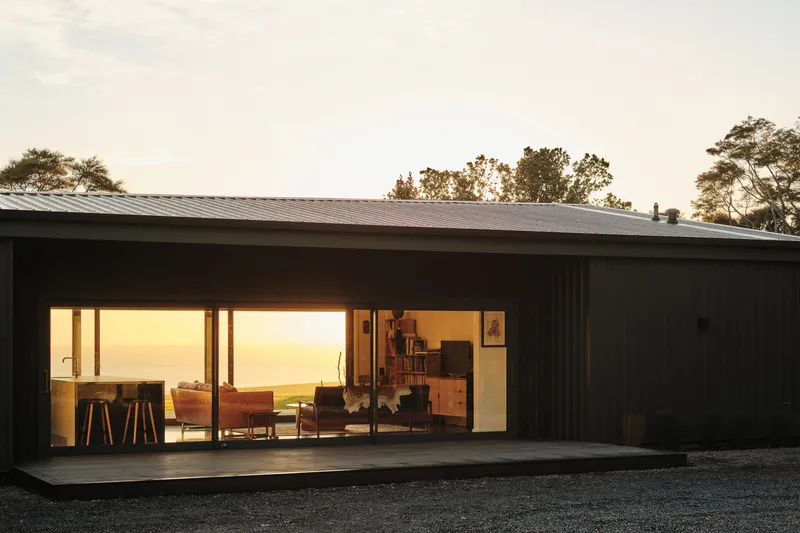 Living pavilion with black timber cladding and full-width glass opening at golden hour