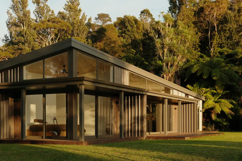 Glass pavilion with timber batten screens and dark metal framing set against native bush in afternoon light