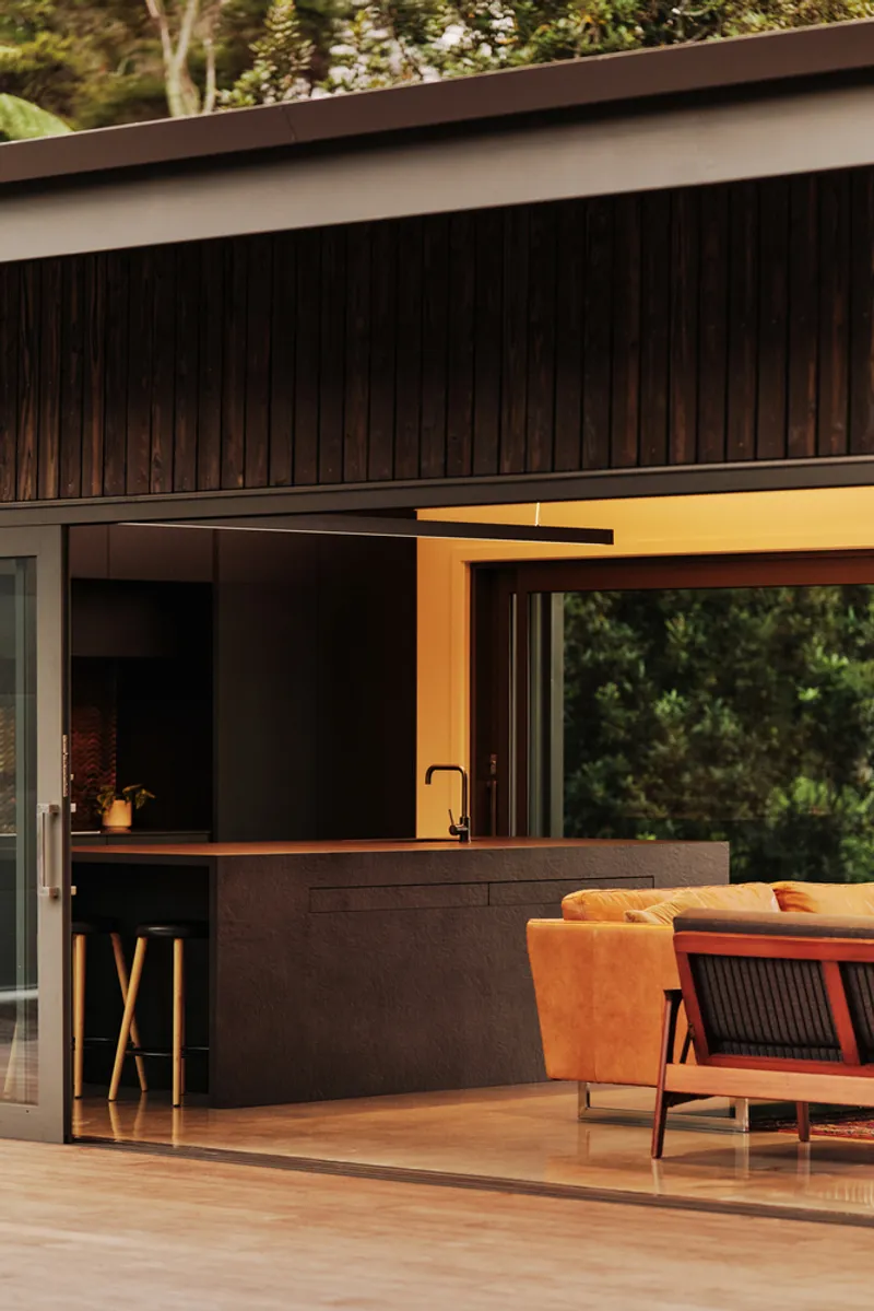 Covered timber deck with outdoor kitchen counter and dark vertical wood siding in afternoon light