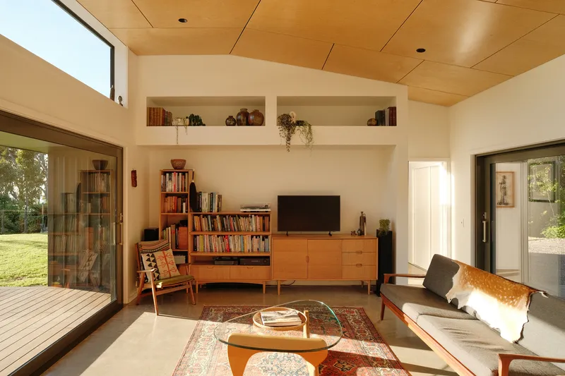 Living room with timber ceiling and built-in media unit flanked by glazed doors to exterior