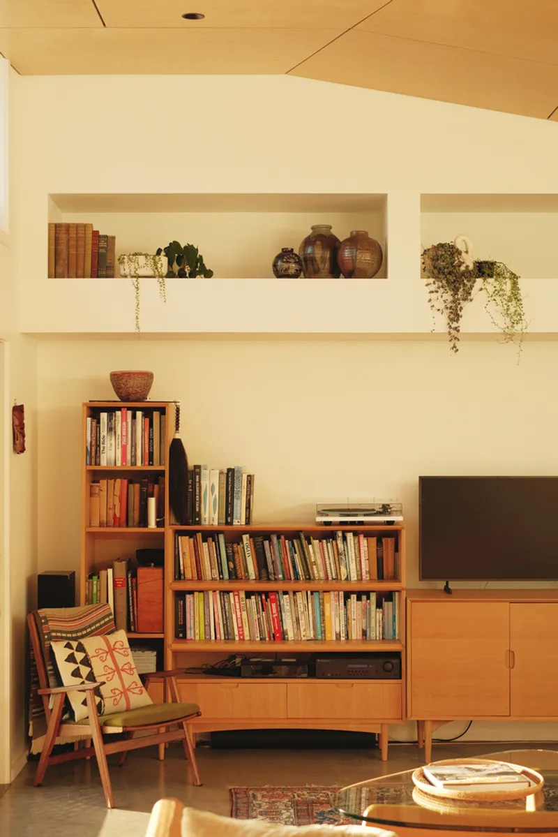 Living room wall with built-in shelving niches holding books and ceramic vessels under timber ceiling