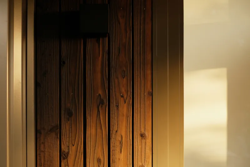 Close-up of vertical timber planking showing grain and knots with afternoon shadow on adjacent wall