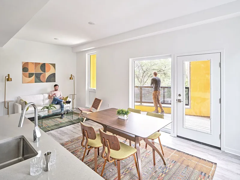 Living and dining area with residents and glazed doors opening to a yellow-walled balcony