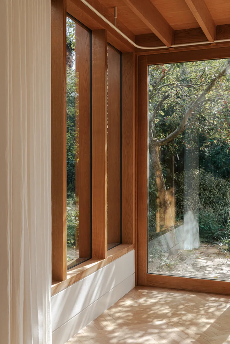 Corner window detail with timber frames and narrow sidelights casting dappled sunlight across the floor