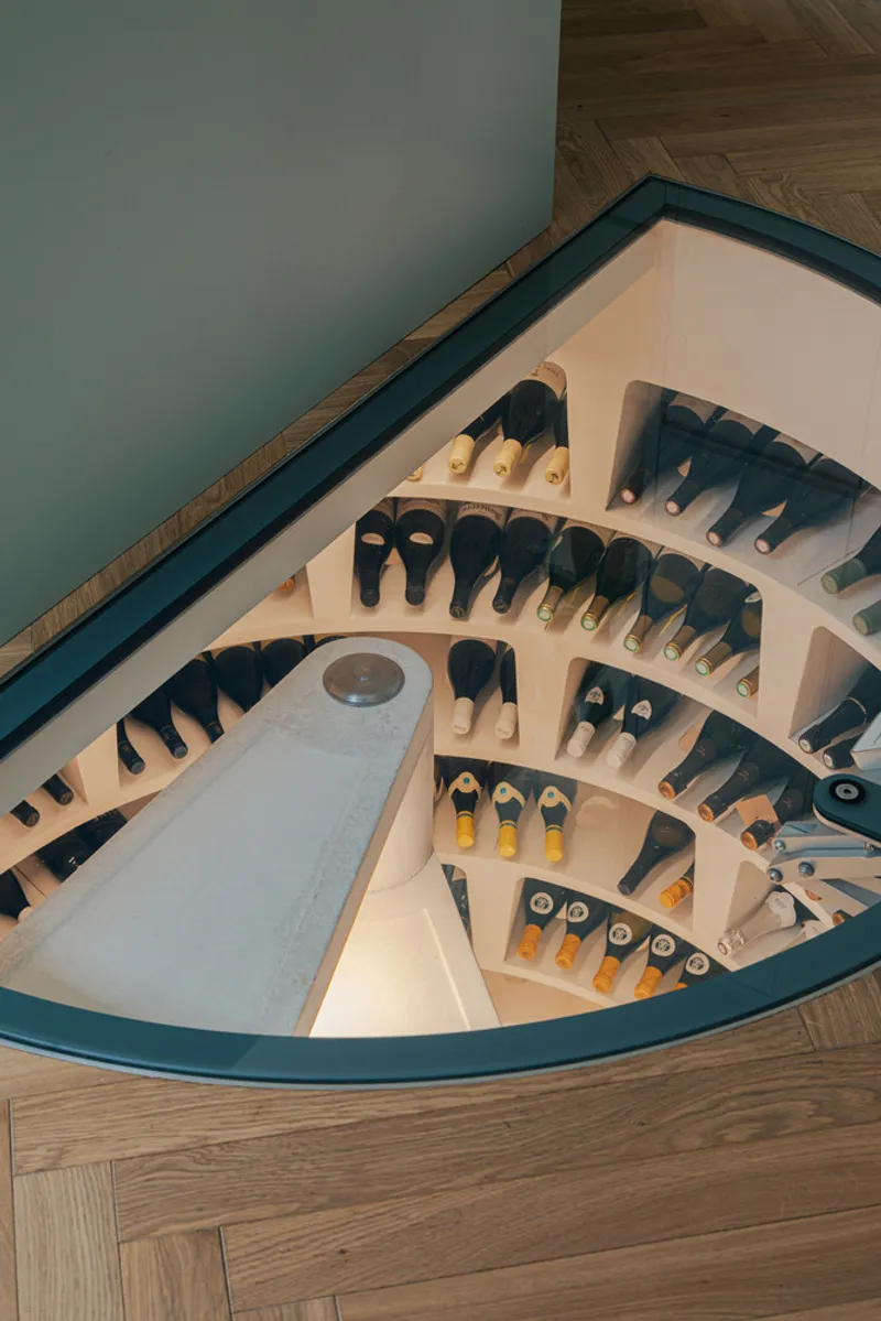 Top-down view of a curved staircase with wine bottles stored in illuminated stepped shelving along the wall