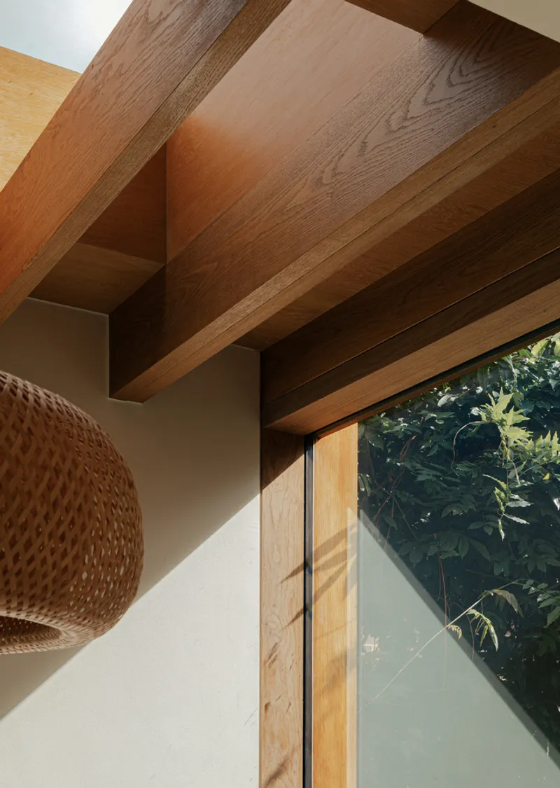 Exposed timber beams meeting at a corner above a glazed door with views to garden foliage