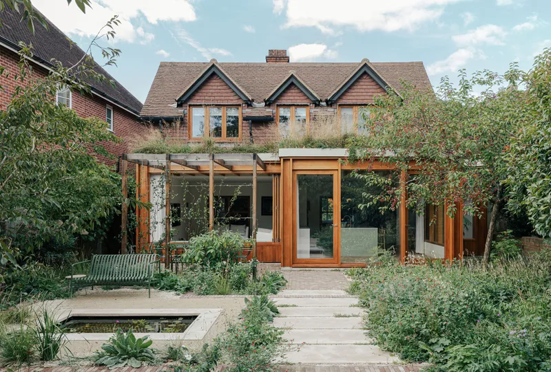 Garden view of timber-framed extension with pergola and wildflower planting beneath a blue summer sky