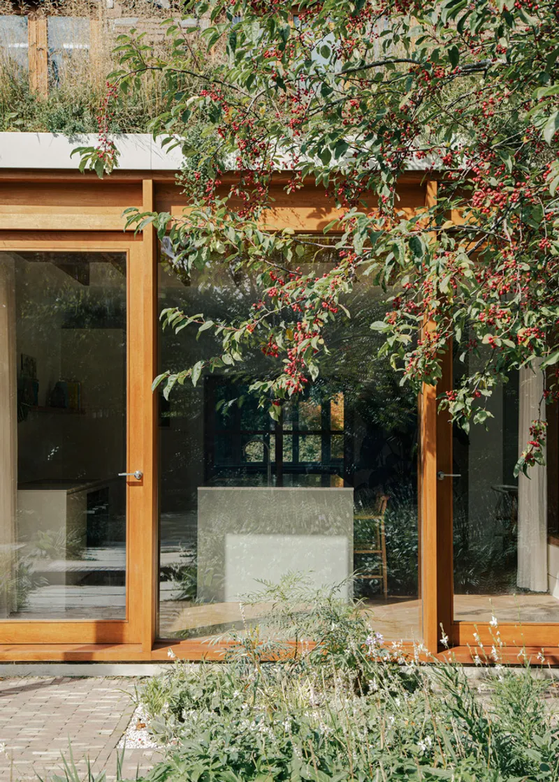 Glazed timber doors framing interior concrete plinth with berry-laden branches overhead