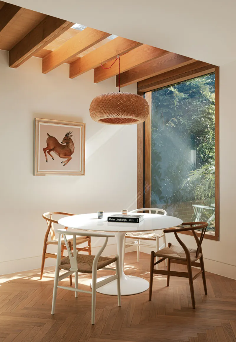 Dining area with exposed timber joists and tall window framing sunlit greenery outside