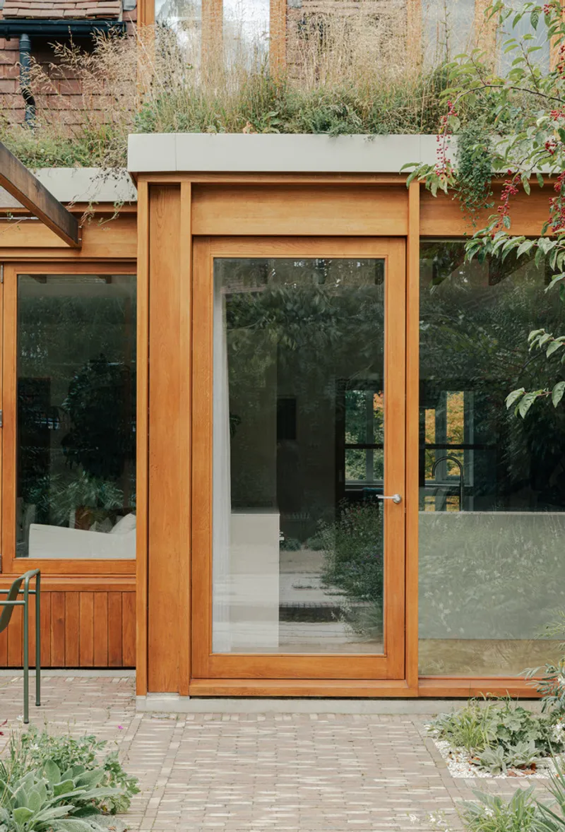 Timber-framed entry door with planted green roof edge and brick paving below
