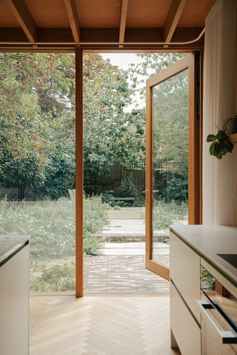 Open pivot door framing a brick path through wildflower meadow planting beyond the interior threshold