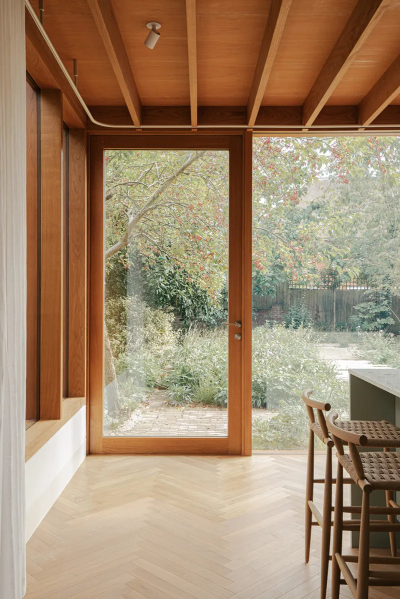 Glazed door with timber frame and herringbone oak flooring opening to garden with woven dining chair