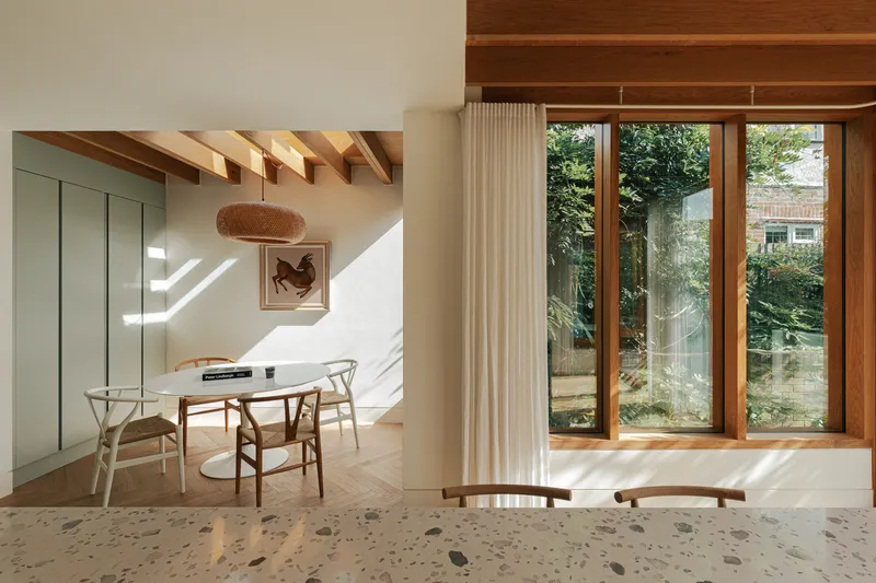 Dining area with timber windows and terrazzo flooring adjacent to kitchen under angled ceiling beams