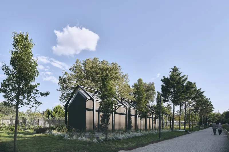 Black gabled pavilion structures with open steel frames amid gravel path and planted landscape