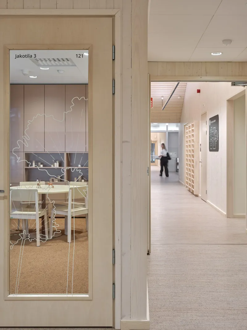 Glass door with etched tree motif and signage leading to a bright corridor