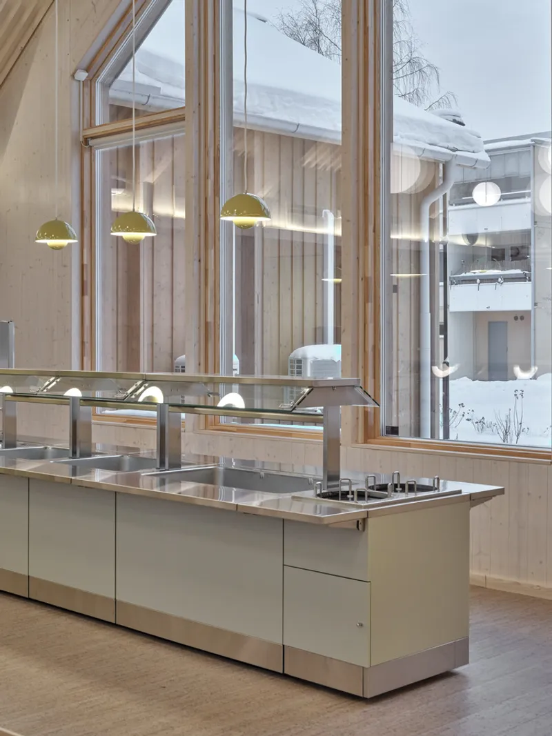 Double-height kitchen with pendant lights and full-height windows overlooking snowy courtyard