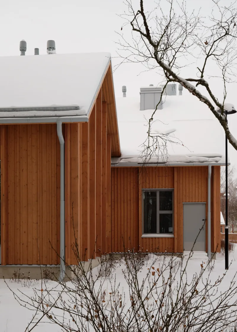 Clustered timber volumes with snow-covered pitched roofs and a bare tree in the foreground