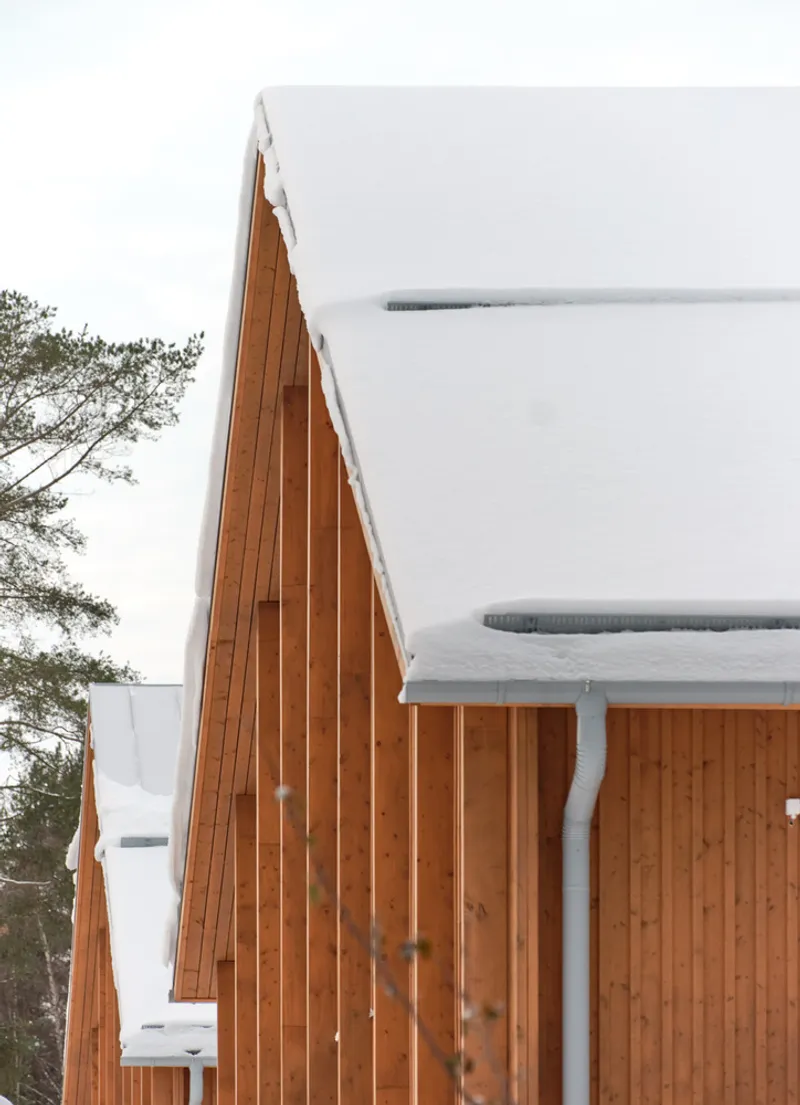 Peaked roof junction with vertical timber cladding and snow accumulation during winter snowfall