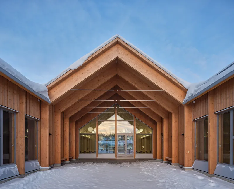 Covered courtyard entry framed by laminated timber arches leading to glazed doors in winter light