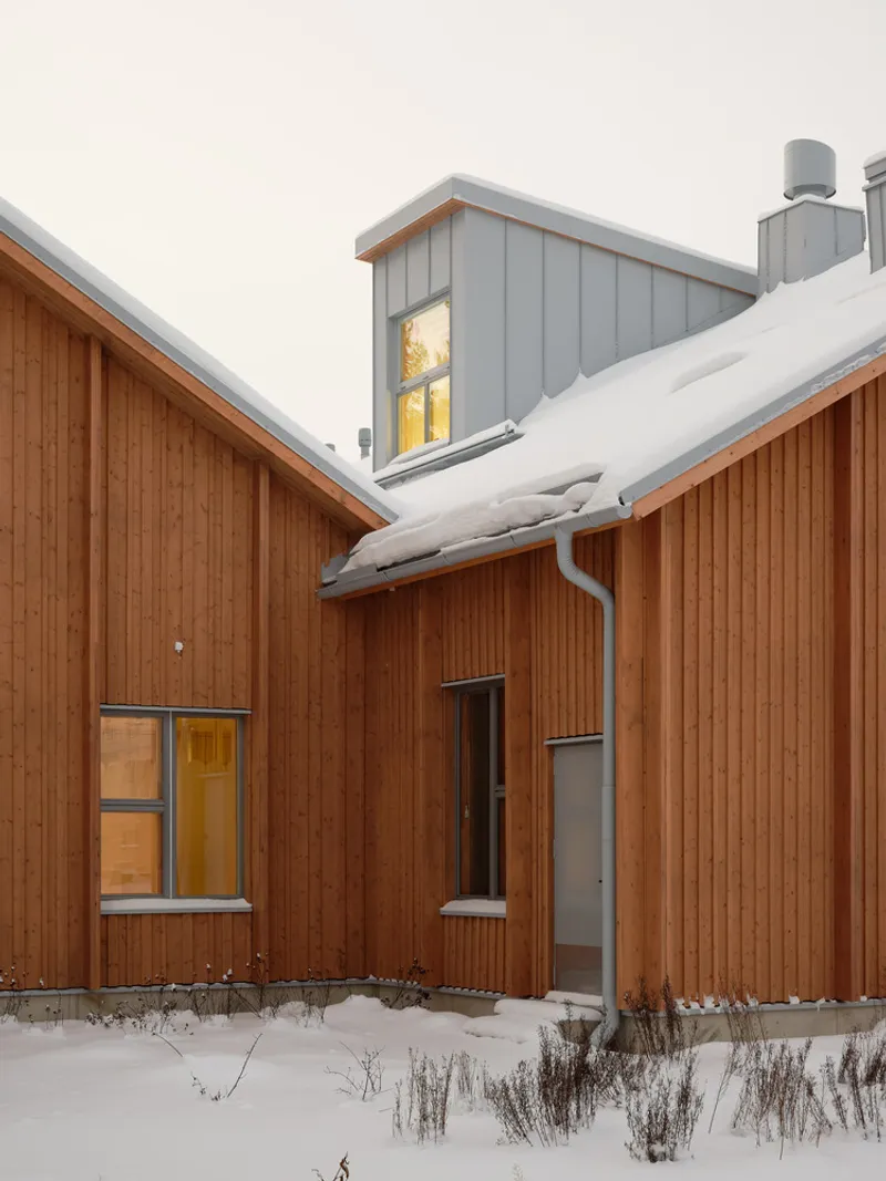 Timber-clad courtyard facade with illuminated windows at dusk and snow on the ground