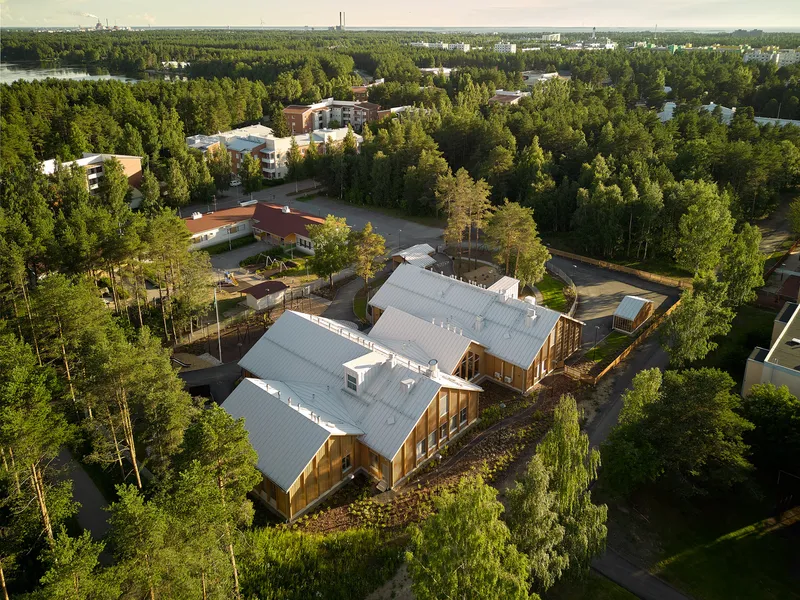 Aerial view of interconnected gabled volumes with standing seam metal roofs nestled in a forested residential area