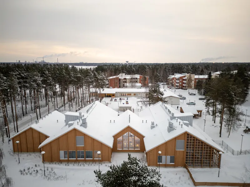Aerial view of timber-clad gabled volumes with snow-covered roofs nestled among pine trees