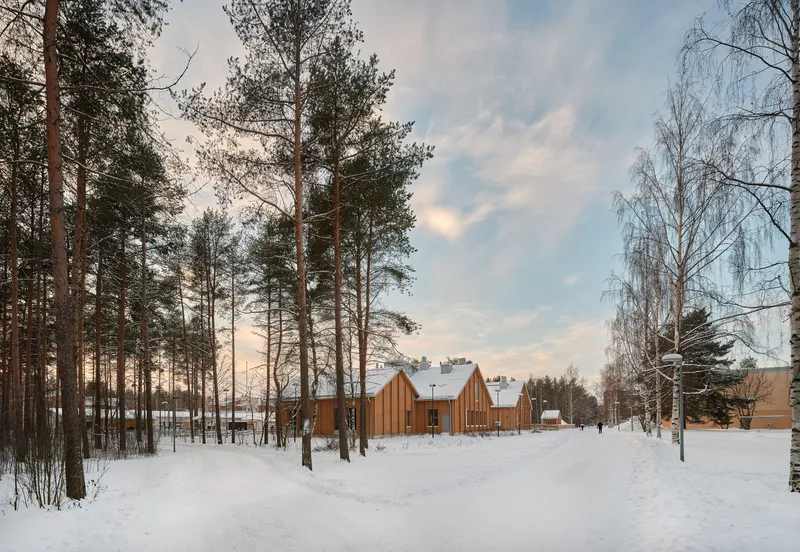 Approach through snow-covered forest path showing the gabled timber facades at dusk