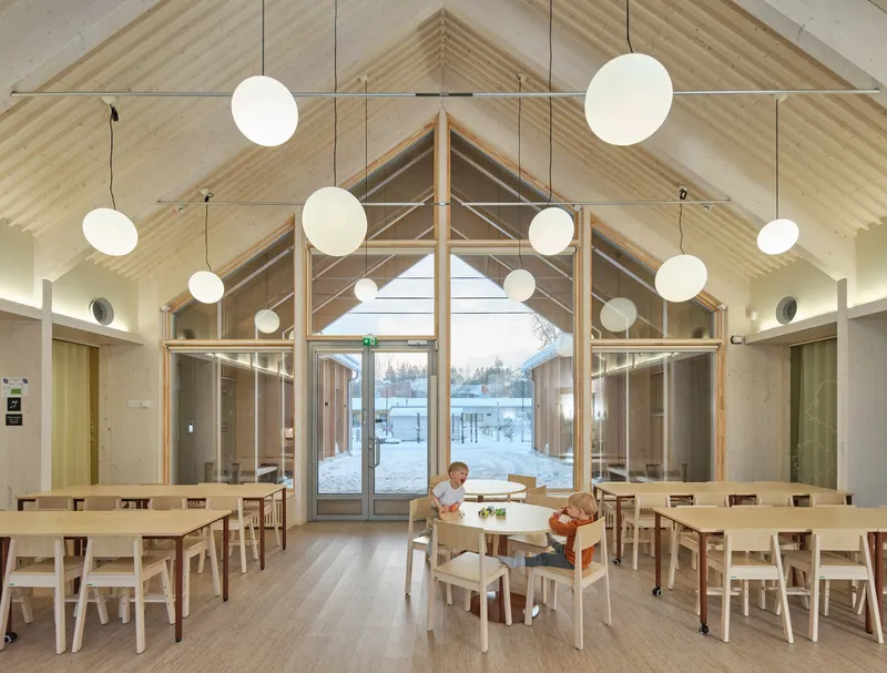 Dining hall interior with exposed timber rafters, globe pendant lights, and children seated at tables