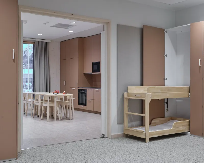 View through doorway to dining area with light wood table and chairs beside kitchen cabinets