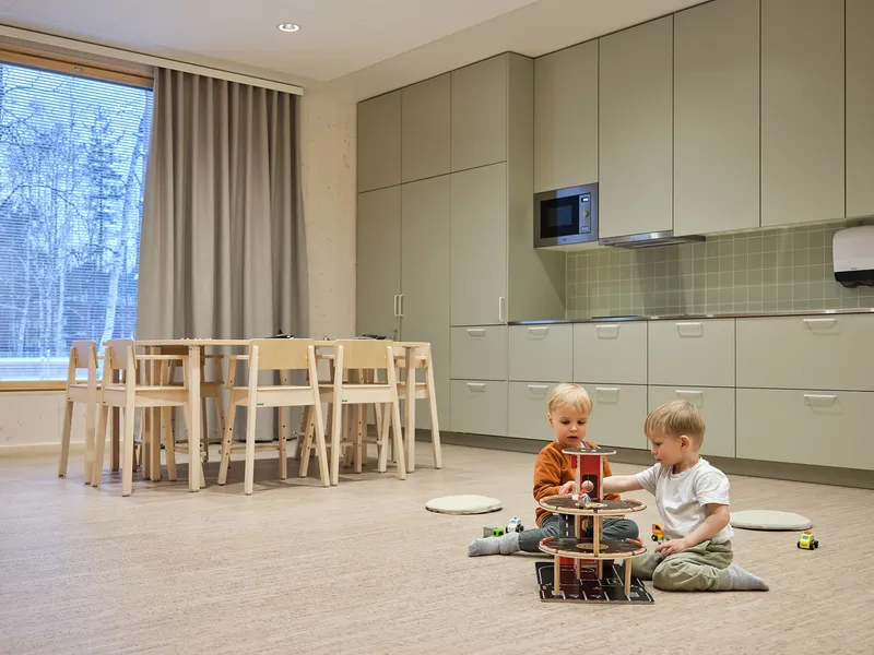 Kitchen and dining space with pale green cabinets, tiled backsplash, and two children playing on floor