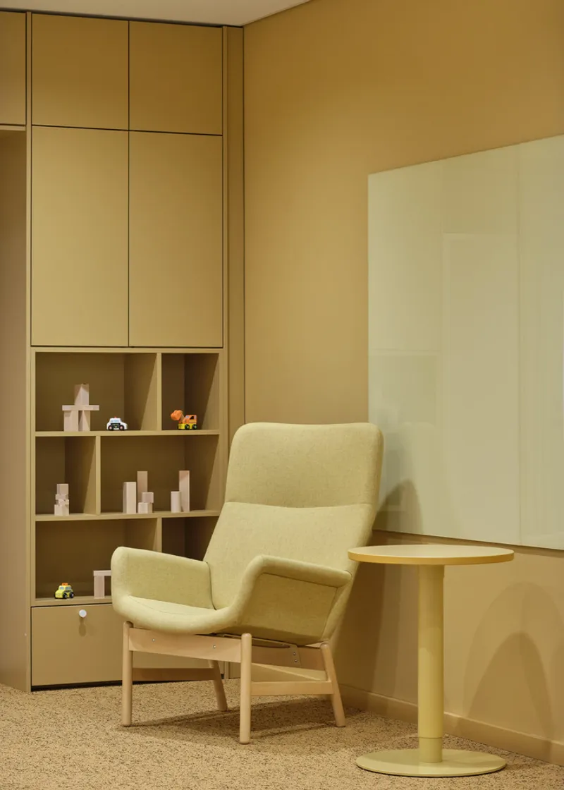 Pale green upholstered armchair beside open shelving with toys and a round side table
