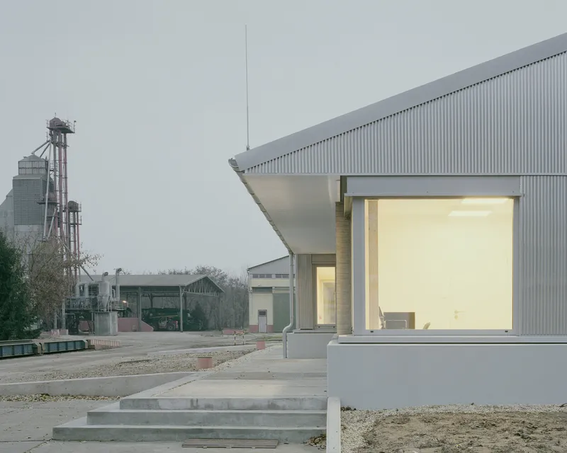 Corrugated metal facade with large glazed opening on a concrete base within an industrial compound