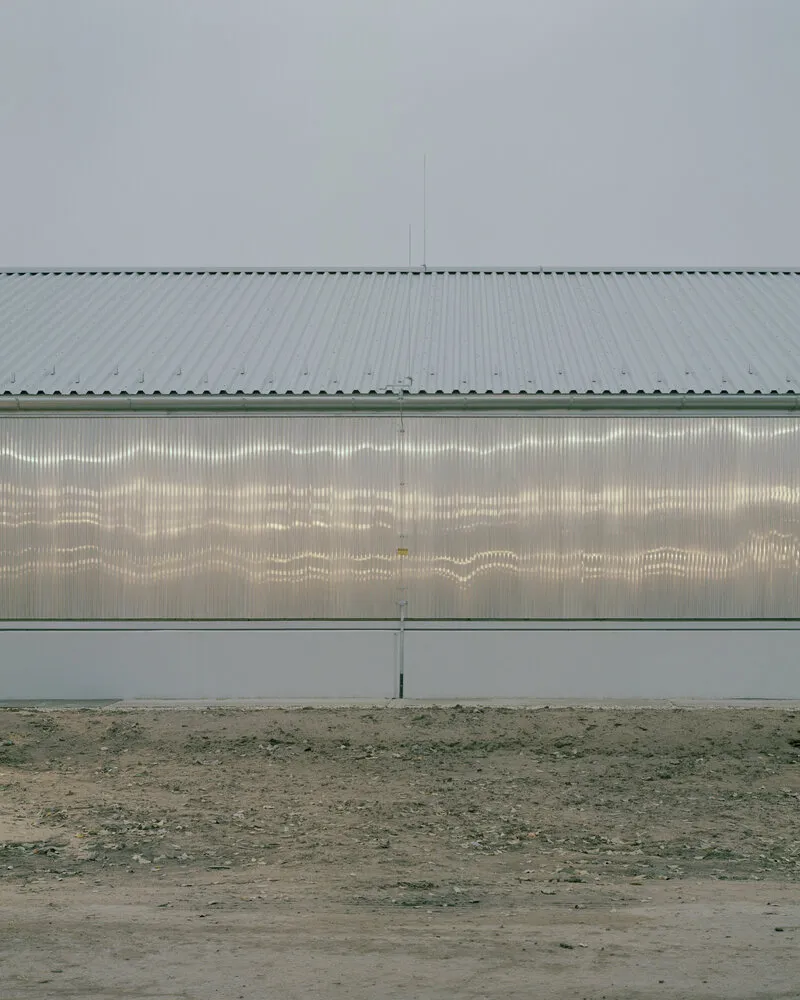 Translucent corrugated wall panel beneath a metal roof with gravel ground in overcast light