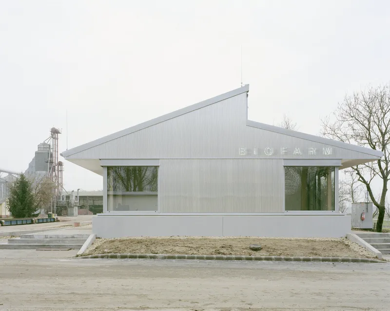 Gabled corrugated metal facade with horizontal strip windows and wide overhanging eaves beside bare trees
