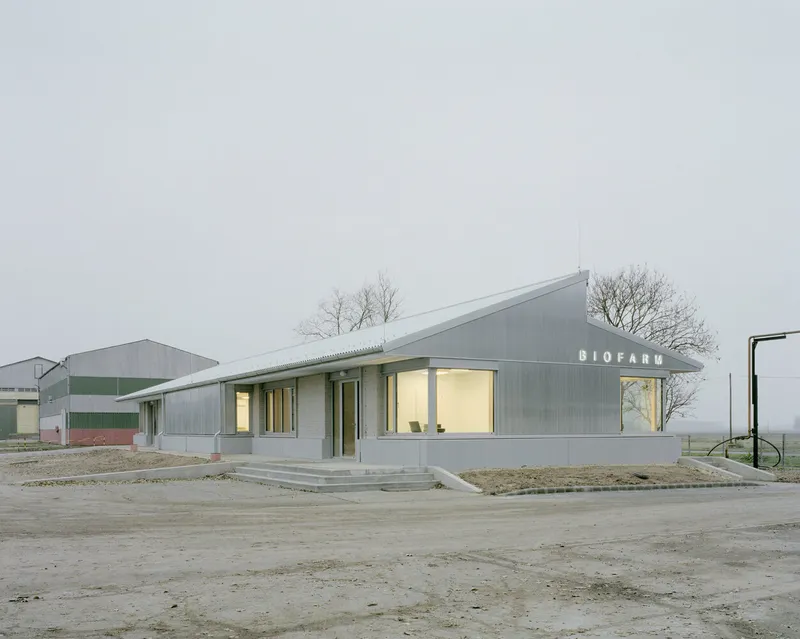 Corner entrance with projecting canopy and glazed opening in corrugated metal volume at dusk
