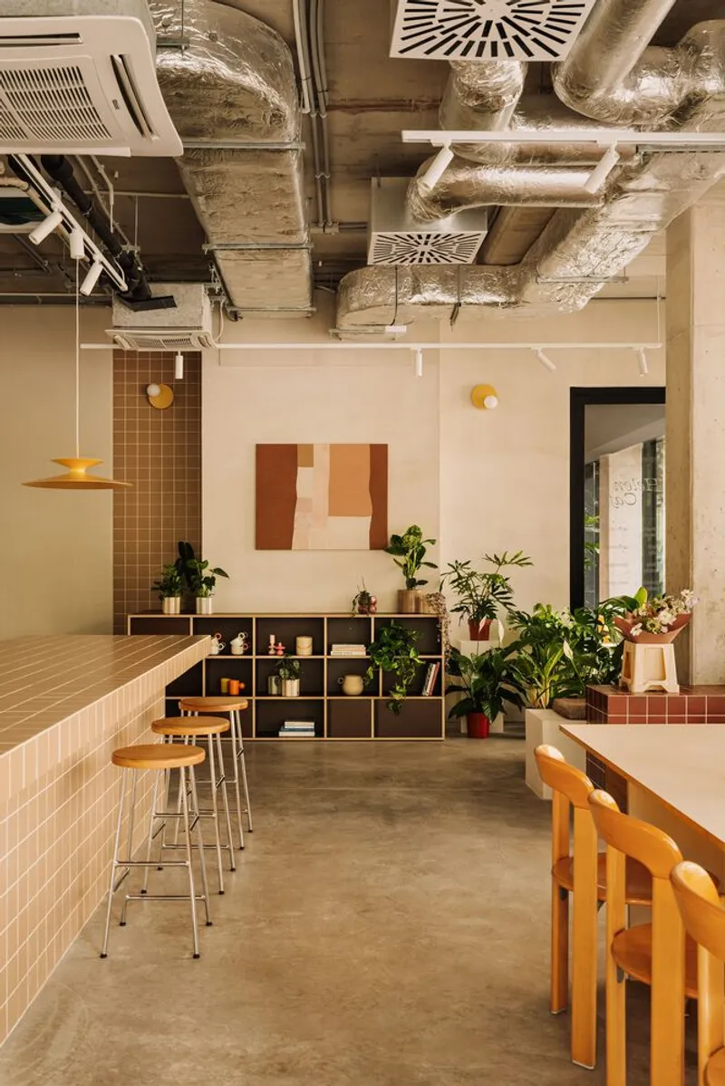 Interior showing exposed concrete ceiling with ventilation ducts above modular shelving and tiled counter with bar stools