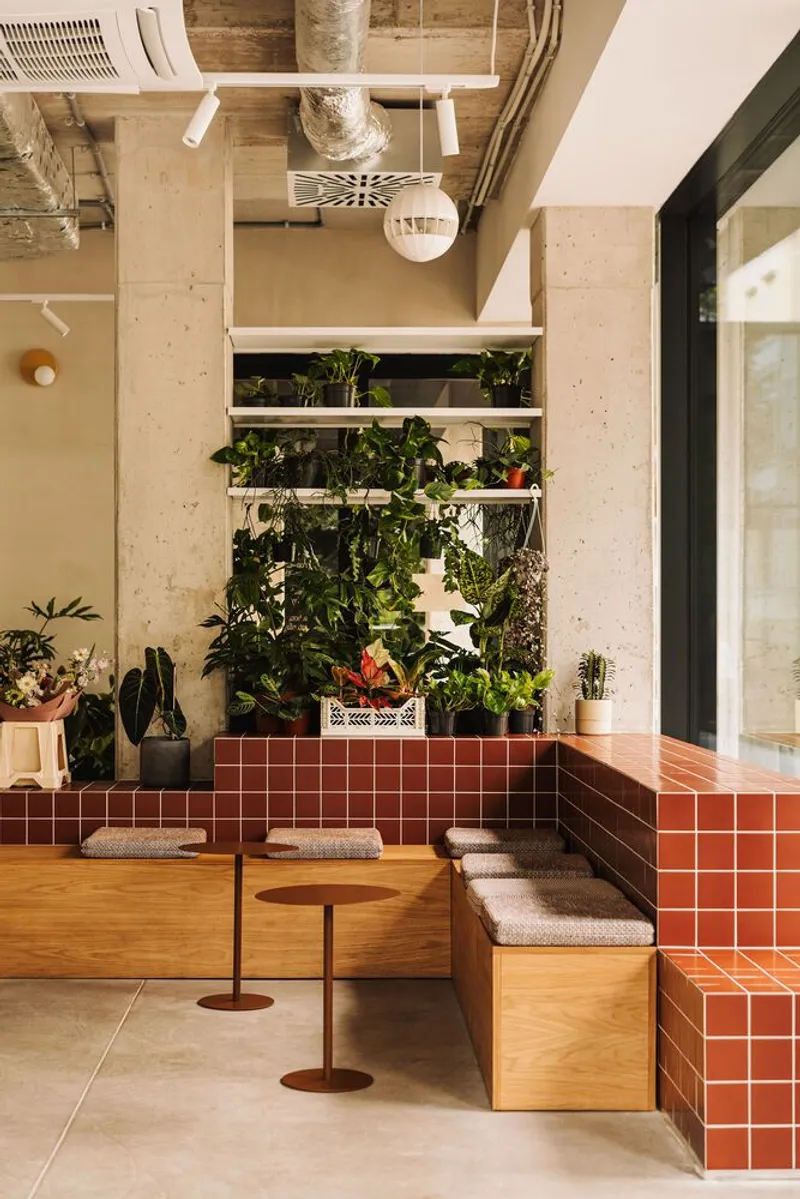 Timber bench seating with terracotta tile base beneath a vertical planted wall and exposed structural ceiling