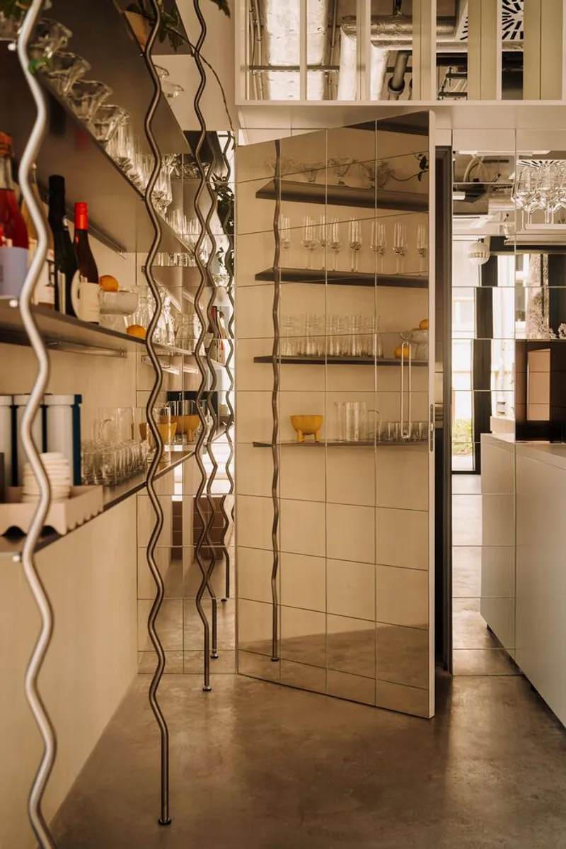 Mirrored glass doors and serpentine metal shelving with glassware under warm interior lighting