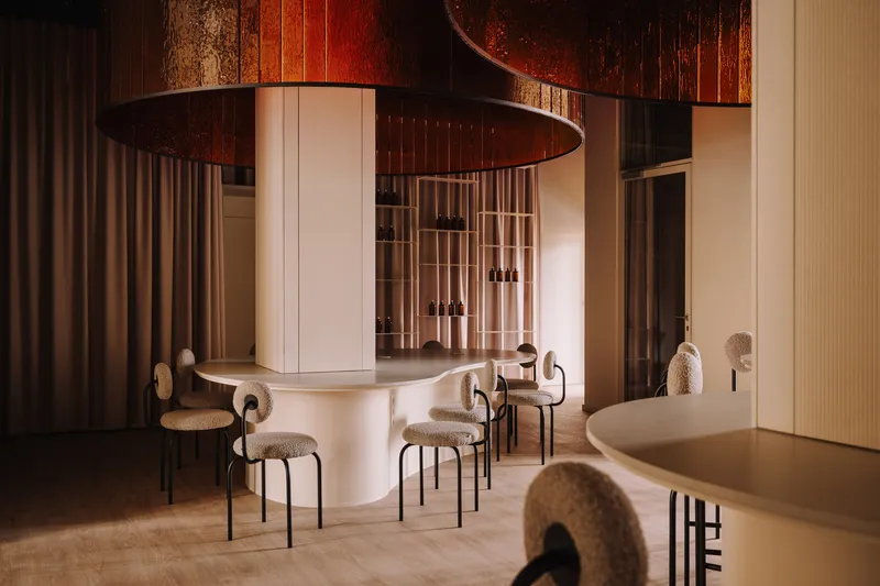 Central bar with curved counter and upholstered stools beneath large oxidized copper pendant lights