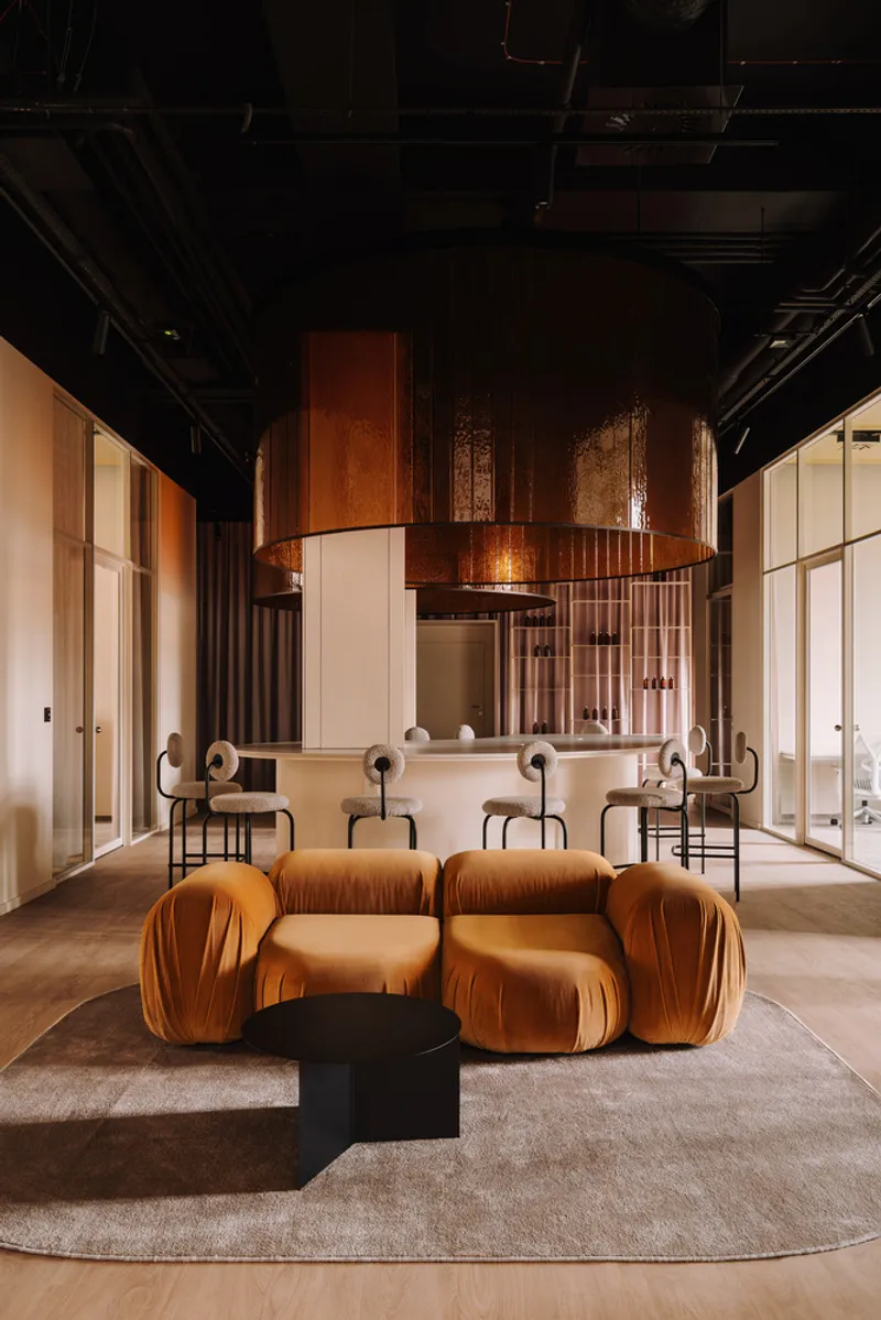Lounge area with velvet seating modules and black coffee table facing the bar under exposed ceiling