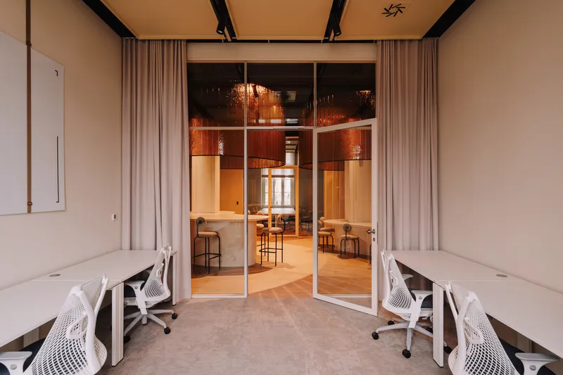 White workspace with desks and task chairs viewing through glass doors to the bar area