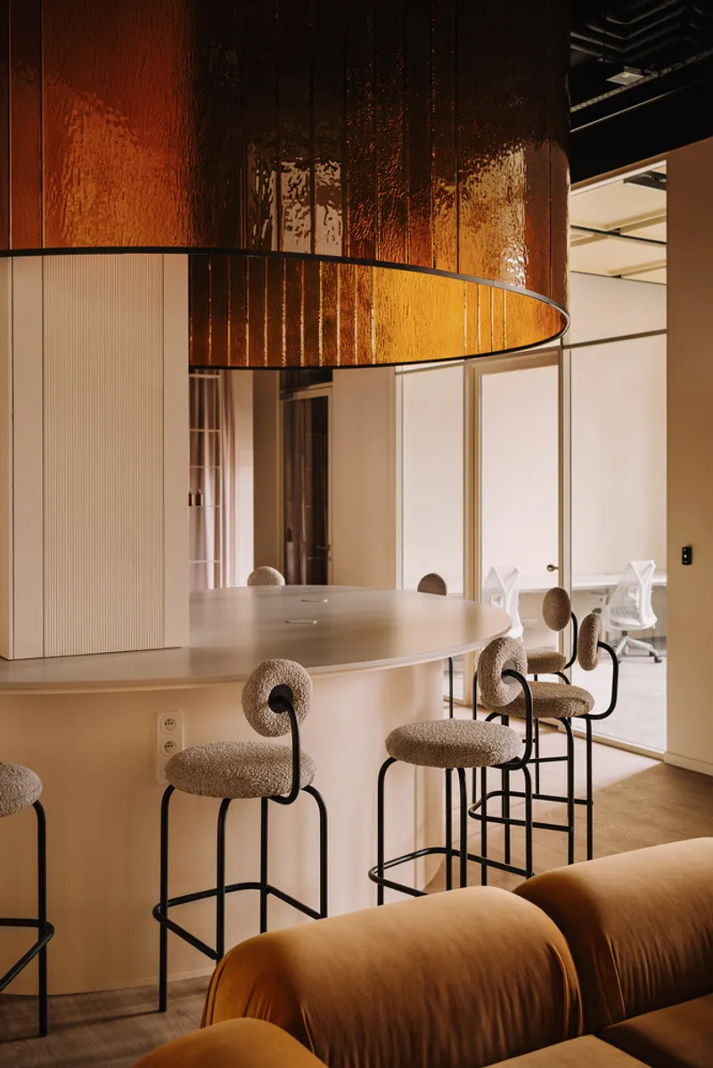 Bar counter with upholstered stools beneath curved timber pendant light and exposed ceiling