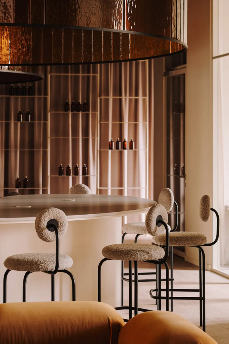 Bar counter with upholstered stools facing a curved mirrored wall with integrated product shelving