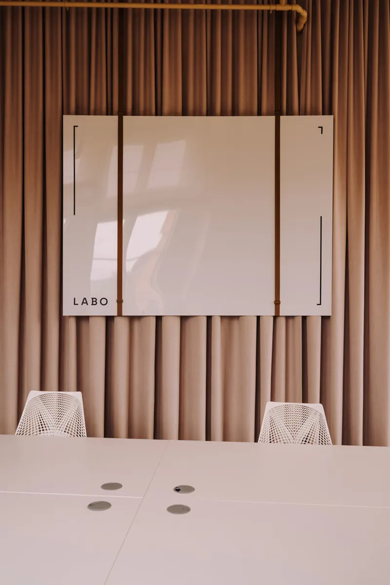 White table surface with mesh chairs facing a frosted glass display panel against pleated fabric wall