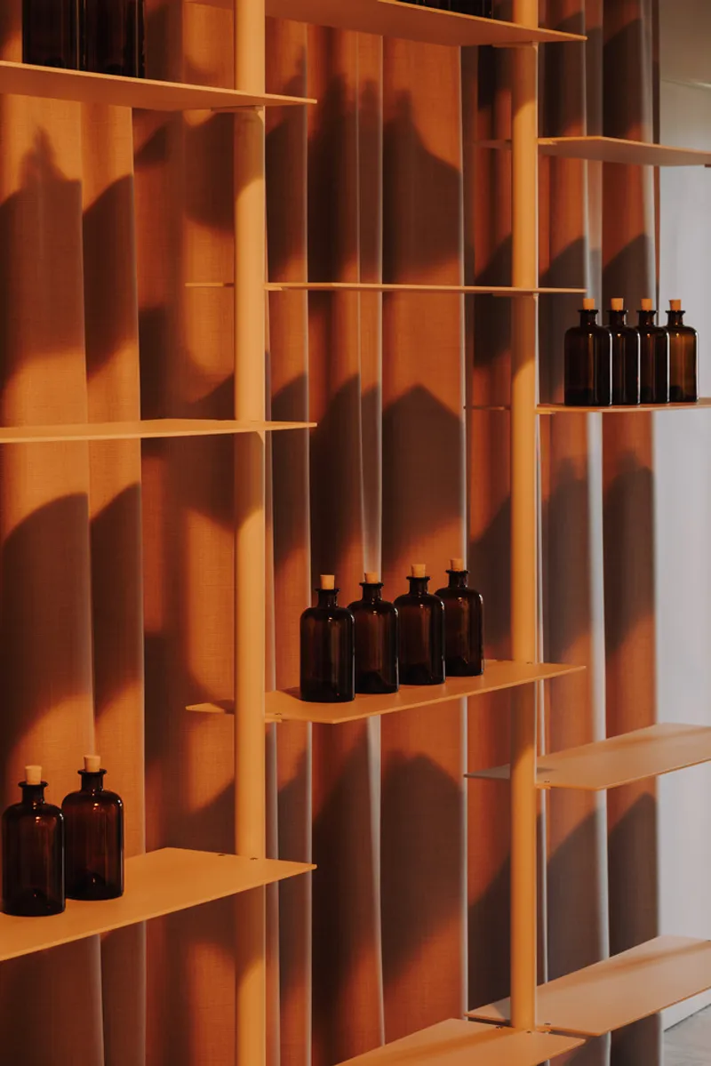 Open timber shelving system with amber glass bottles illuminated by warm afternoon sunlight and shadows